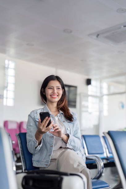 istock Cheerful young woman waiting in airport lounge while using smartphone for flight information 2195592850