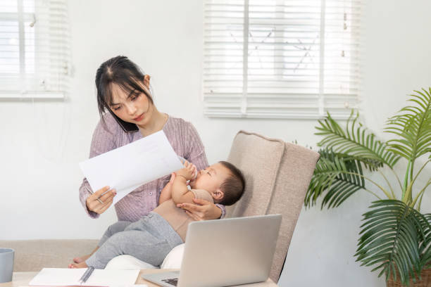 istock Single mom managing her workload while nurturing her baby, reviewing documents at home 2195592876