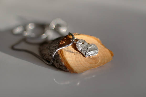 istock Beautiful handmade silver heart-shaped pendant with intricate leaf texture on wooden background. 2195596805