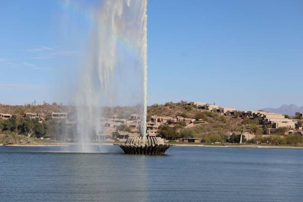 The iconic fountain at Fountain Hills, Arizona, shoots water high into the clear blue sky, surrounded by desert landscape and residential homes.