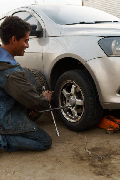 Young mechanic changing a flat tire on a car parked on the side of a dirt road