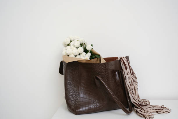 This elegant brown handbag, adorned gracefully with exquisite white flowers hanging on white table.