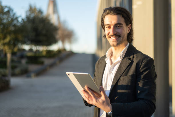 istock Successful Businessman Holding Tablet Confidently Near Modern Office Building, Authentic Online Communication And Work Portrait. 2195611335