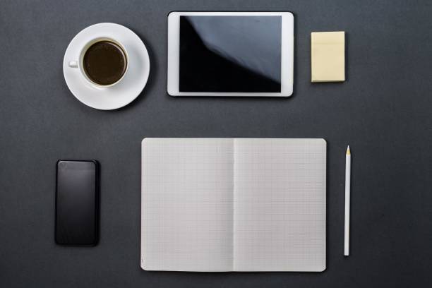 Black desk with coffee, tablet, notebook, pencil, and smartphone