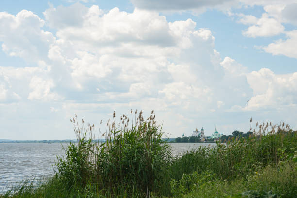 Green trees by the lake on a sunny day, with clouds on the sky. Orthodox monastery in the background. High quality photo