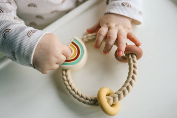 istock Baby holding a silicone rainbow teether with braided handle and pastel-colored details. Perfect for sensory play and teething relief. Modern and functional design 2195619214