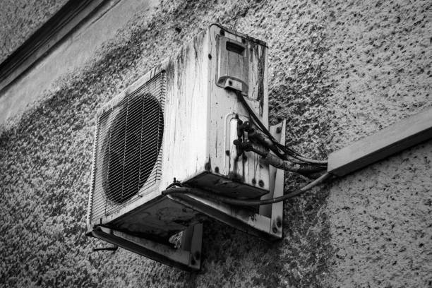 Old air conditioning unit mounted on a textured wall in black and white photography