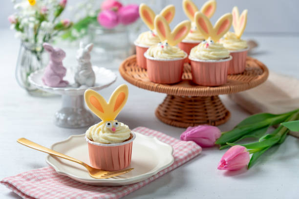 Carrot cake cupcakes for Easter. Carrot cupcakes with cream cheese frosting decorated with easter bunny ears on white wooden background.