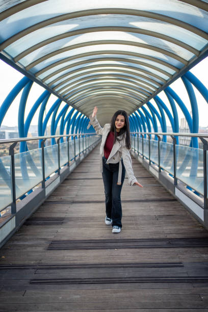Stylish young woman waving while walking on a modern pedestrian bridge located in Móstoles