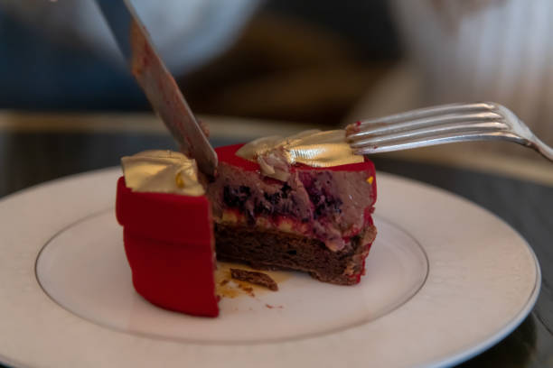 A vibrant red dessert with a glossy finish is being cut in a chic cafe. The rich layers reveal chocolate and berry filling, enticing those nearby to savor its flavor.