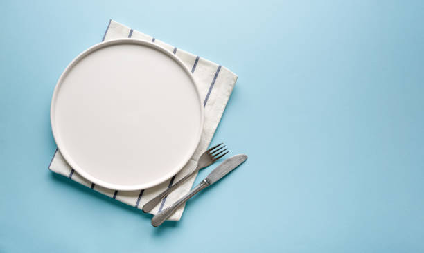istock Top view of empty ceramic white plate and cutlery on blue background 2195637313