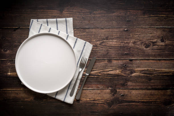istock Top view of empty ceramic white plate, fork and table knife on wooden table 2195637626