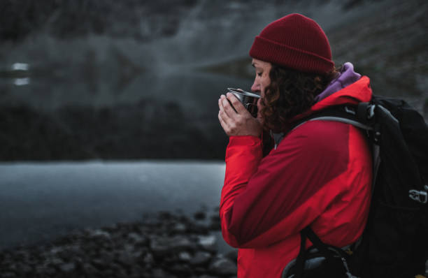 istock Woman in Red Jacket Drinking Hot Coffee by Lake 2195639419