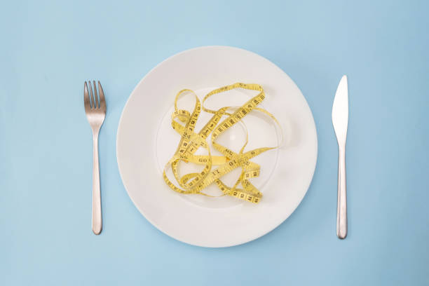 Diet and Calorie Control Concept: White Plate with Yellow Measuring Tape, Fork and Knife on Blue Background