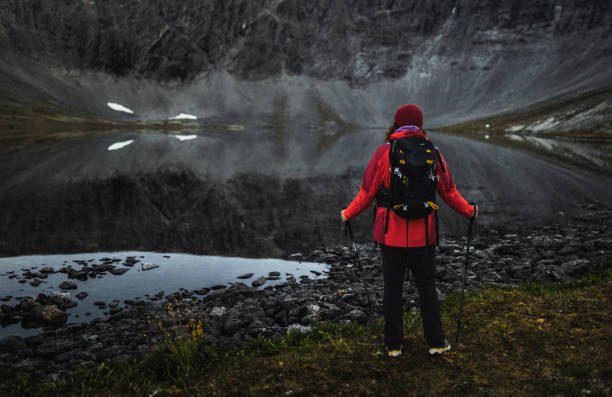 istock Hiker standing by a reflective lake in a serene mountain landscape 2195639660
