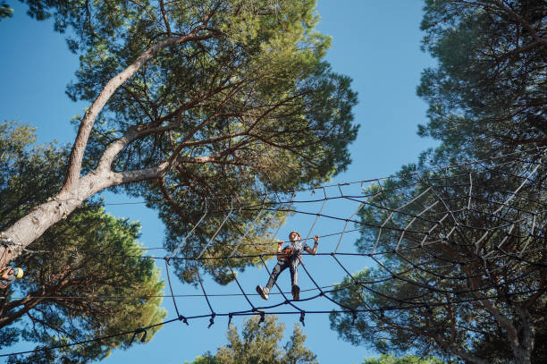 Teen boy bravely walks on the rope web in adventure park. Safe climbing with helmet and insurance. Child in adventure park in forest, extreme sport