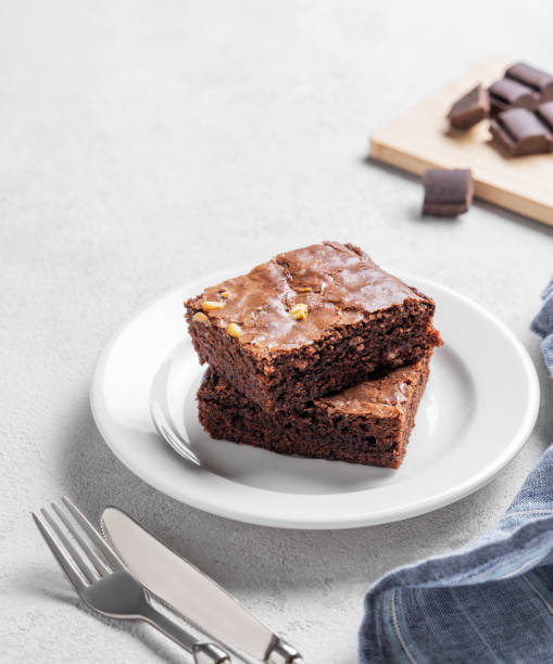 istock Chocolate brownie with nuts cut into pieces on a plate on a light background with fork and napkin. 2195651827