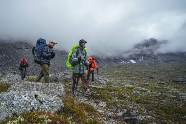 Hikers with backpacks traverse rugged, rocky terrain enveloped in mist, showcasing adventure and nature.