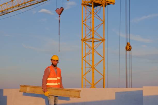 istock Construction worker carrying wooden plank on rooftop at sunset 2195656270
