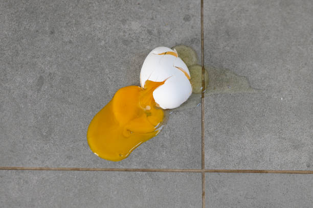 Cracked egg spills its vibrant yolk on a gray tiled surface in a quiet kitchen setting