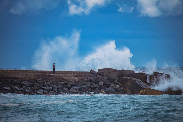 Balancing on the rocky shoreline, a man enjoys the solitary pursuit of fishing, his silhouette a testament to the tranquility and focus of this outdoor pastime.