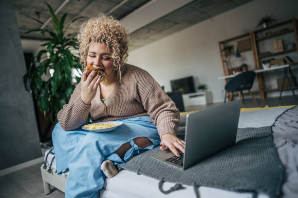istock A chubby woman enjoying burger while relaxing in bedroom 2195664881