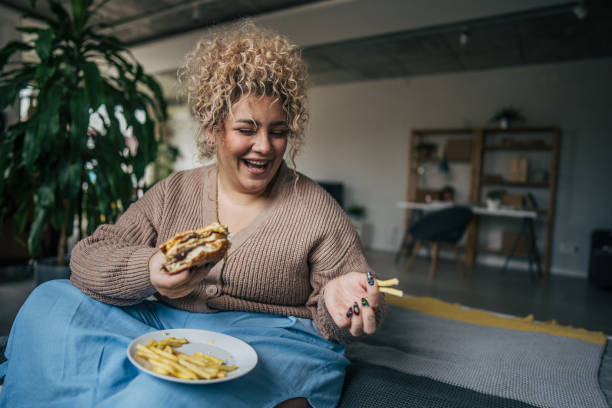 istock A chubby woman enjoying burger while relaxing in bedroom 2195664990