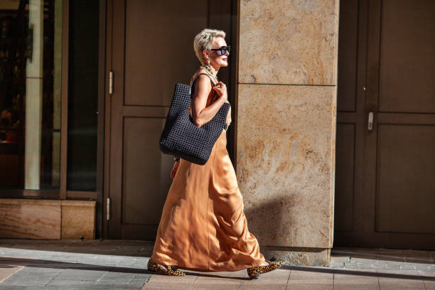 Stylish Mature Woman with Short Hairstyle Walks, Wearing Summer Beige maxi Dress and Large Handbag. Fashion Mode in City Stylish Mature Woman with Short Hairstyle Walks, Wearing Summer Beige maxi Dress and Large Handbag. Fashion Mode in City. older woman purse stock pictures, royalty-free photos & images