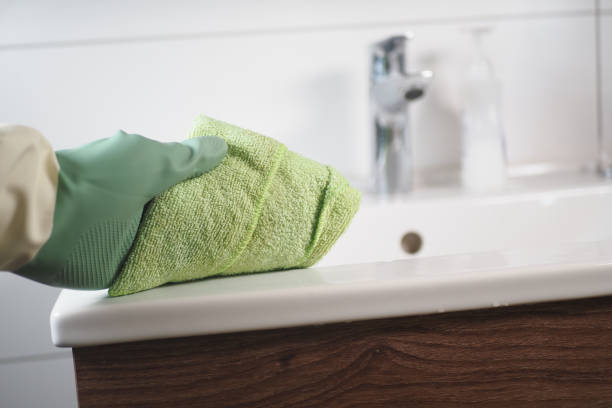 An individual is diligently cleaning a bathroom sink using a green microfiber cleaning cloth