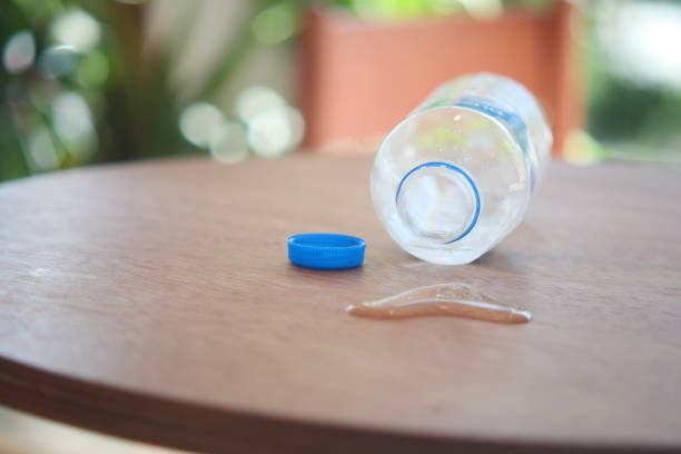 A tippedover plastic water bottle, with its cap placed beside it, is resting on a wooden table