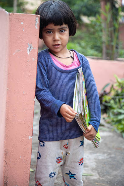 A young girl stands outdoors near a wall, holding books, in a peaceful natural setting. The image captures innocence, learning, and a calm atmosphere, suitable for educational or community themes.
