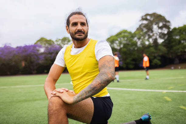 A determined soccer player stretching on a sports field before practice, surrounded by teammates.