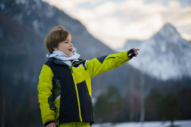 Happy little boy in warm clothing stands on a snowy mountain and points his hand into the distance