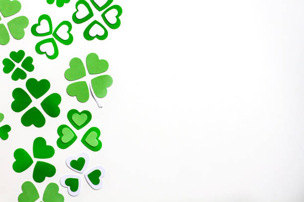 Happy St Patrick's Day banner design with green paper cut leaves clover confetti on white table. Top view, flat lay, copy space. Ideal for greeting card