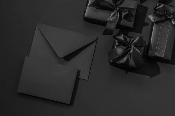 istock Black gift boxes with satin ribbons and a black envelope on a black background. Monochrome greeting card. 2195681741