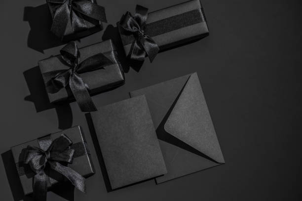 istock Several black gift boxes with satin ribbons and a black envelope on a black background. Monochrome greeting card. 2195681742