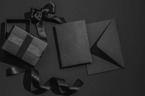 istock Black gift box with satin ribbons and bow and a black envelope on a black background. Greeting card. 2195681753