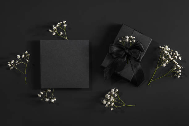 istock Black gift box and black card on a black background with space for text and sprigs of gypsophila. Congratulations, postcard. 2195681790