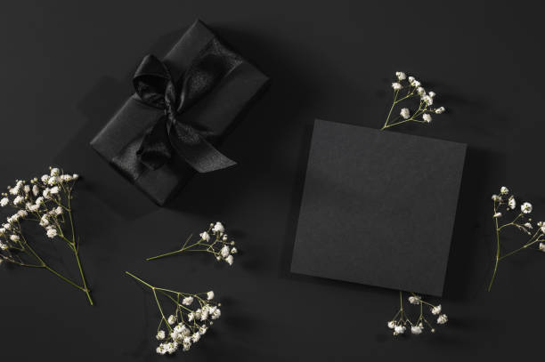 istock Black gift box and black card on a black background with space for text and sprigs of gypsophila. 2195681830