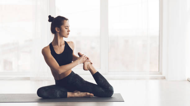 istock Woman Practicing Yoga in a Bright Room With Large Windows While Performing a Stretching Pose 2195695330