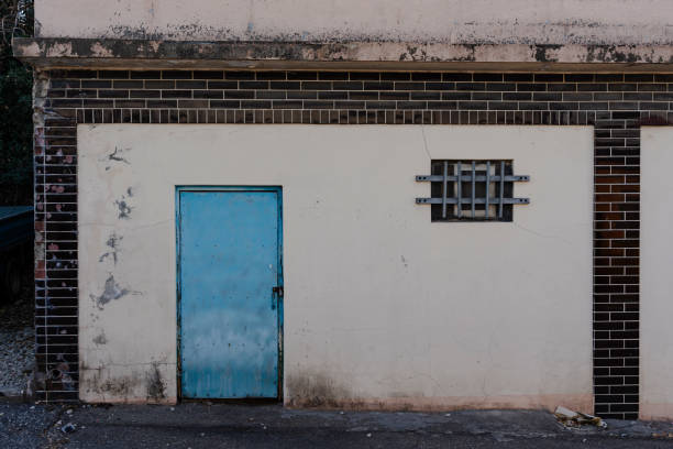 Distressed building exterior. A light blue door, barred window, and aged brick and plaster are featured.