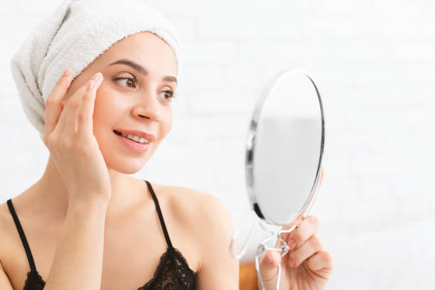istock Woman Applying Skincare While Looking in Mirror After Shower in Bright Bathroom Setting 2195699603