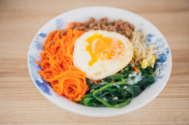 a close-up of korean bibimbap with fresh vegetables, seasoned meat, and a perfectly cooked egg on top. the vibrant colors and textures make it a social-media-worthy culinary masterpiece.