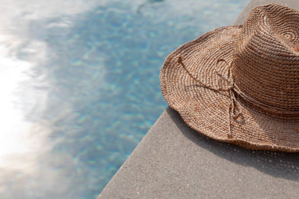 Woven floppy hat on the concrete edge of swimming pool with sun flares and reglections on the water