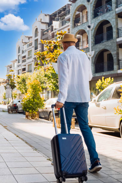 istock traveler strolls down a city sidewalk pulling a suitcase, surrounded by contemporary architecture and greenery. 2195703290