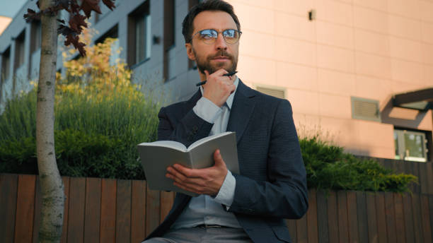 istock Thoughtful pensive man Caucasian businessman business coach in city write notes in notebook university professor writer thinking writing ideas at paper notepad smiling prepare for class lesson outside 2195705302