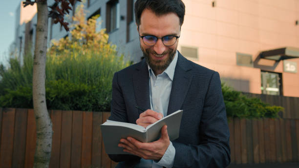 istock Caucasian business man businessman outside thinking writing notes in notebook university teacher professor in city hold paper notepad smile come up with idea creative thought prepare for exam studying 2195718329