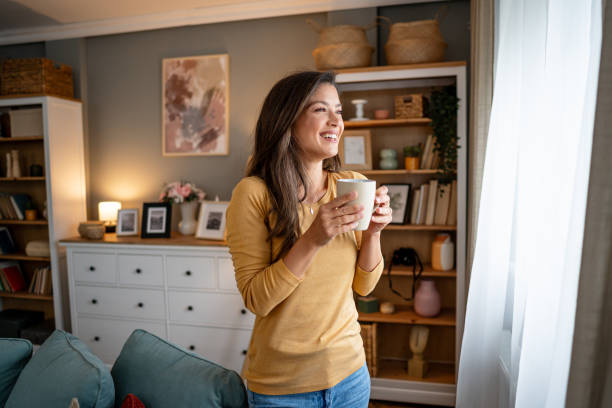 istock Woman with coffee looking through the window 2195721156