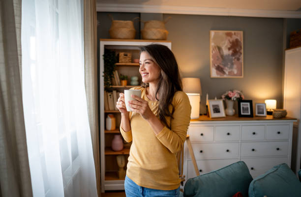 istock Woman with coffee looking through the window 2195721714