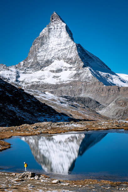 istock Lone Hiker at Matterhorn With Stunning Reflection in Alpine Lake 2195722196